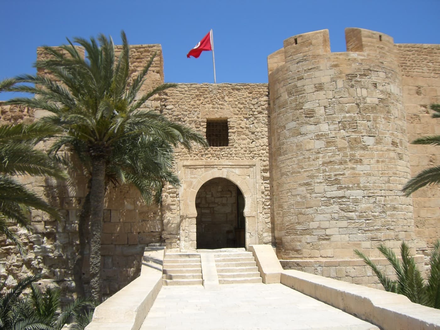 The gate and towers of Borj El Kebir fort in Houmt Souk, with palms and a Tunisian flag
