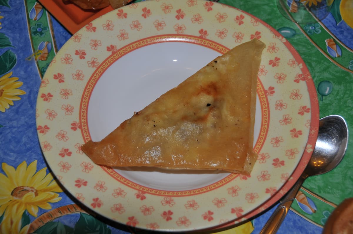 A golden, triangular Tunisian brik on a patterned plate